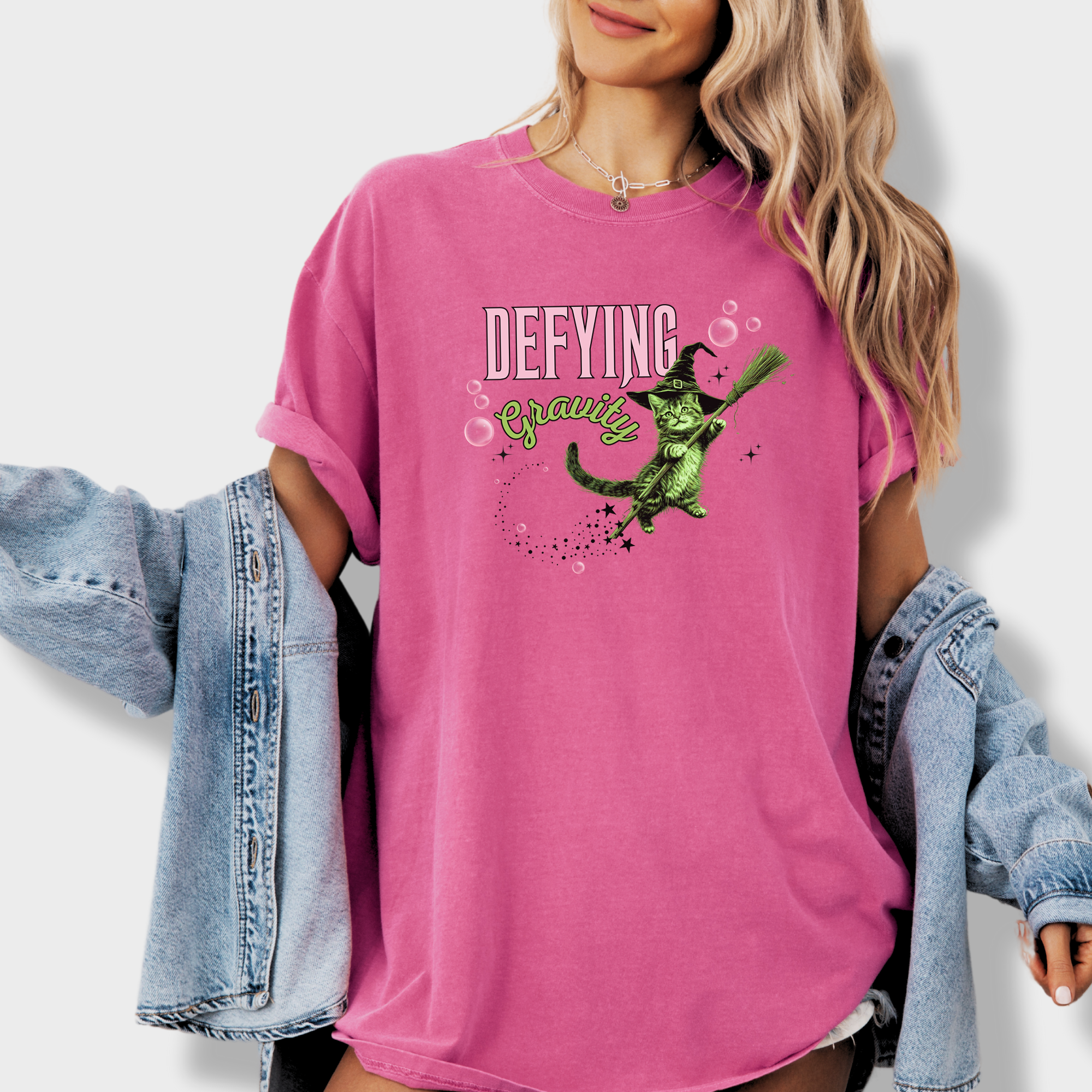 Unique graphic tee showcasing a mystical green witch cat in a levitating pose. A fun retro T-shirt for cat parents and Wicked fans.