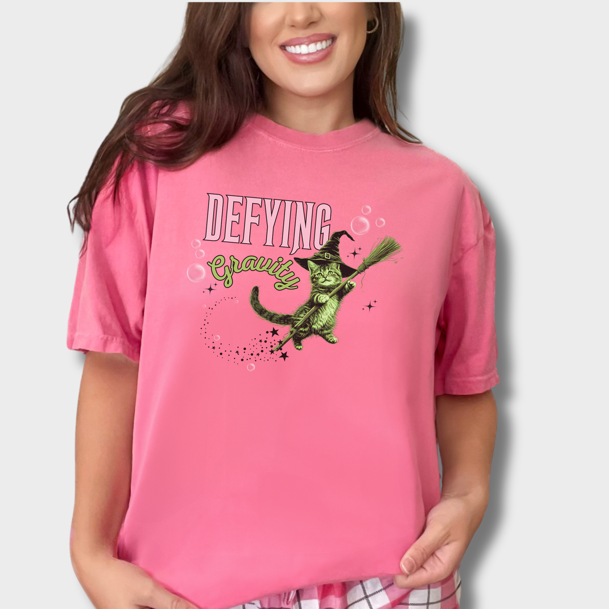 Unique graphic tee showcasing a mystical green witch cat in a levitating pose. A fun retro T-shirt for cat parents and Wicked fans.