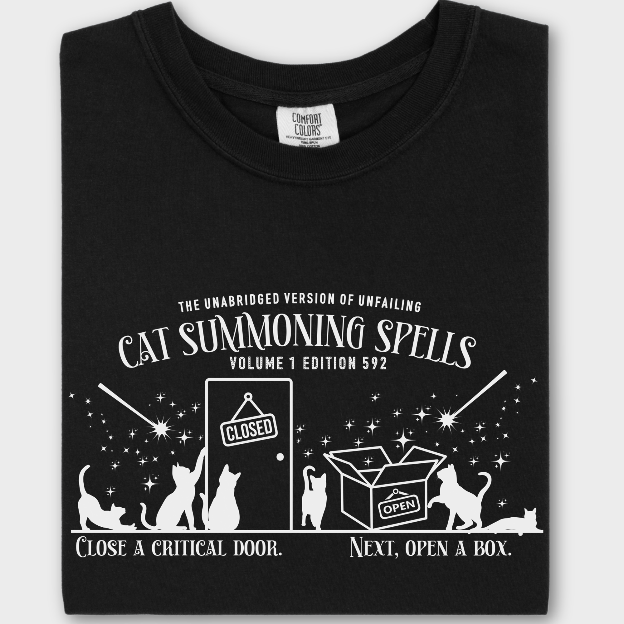 Minimalist cat-themed T-shirt featuring a 'Cat Summoning Spells' book graphic, where wands magically summon cats to doors and boxes.