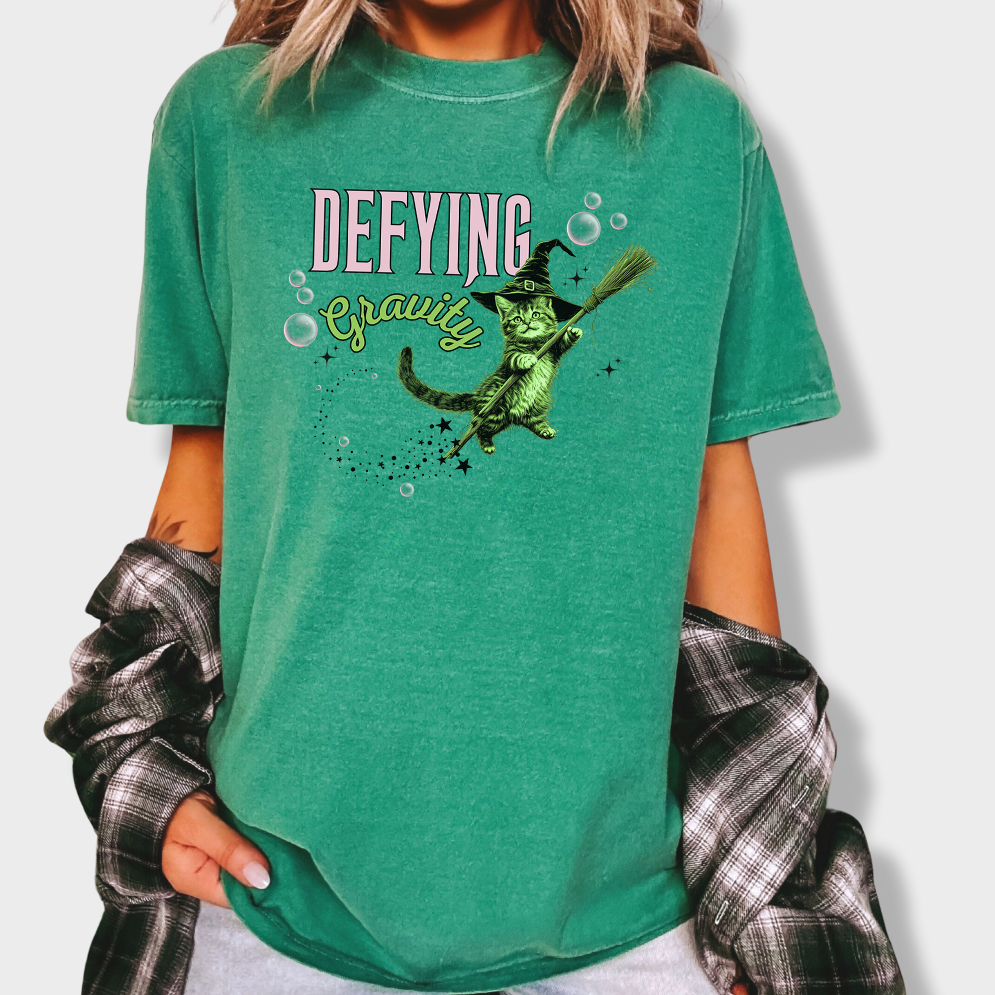 Unique graphic tee showcasing a mystical green witch cat in a levitating pose. A fun retro T-shirt for cat parents and Wicked fans.