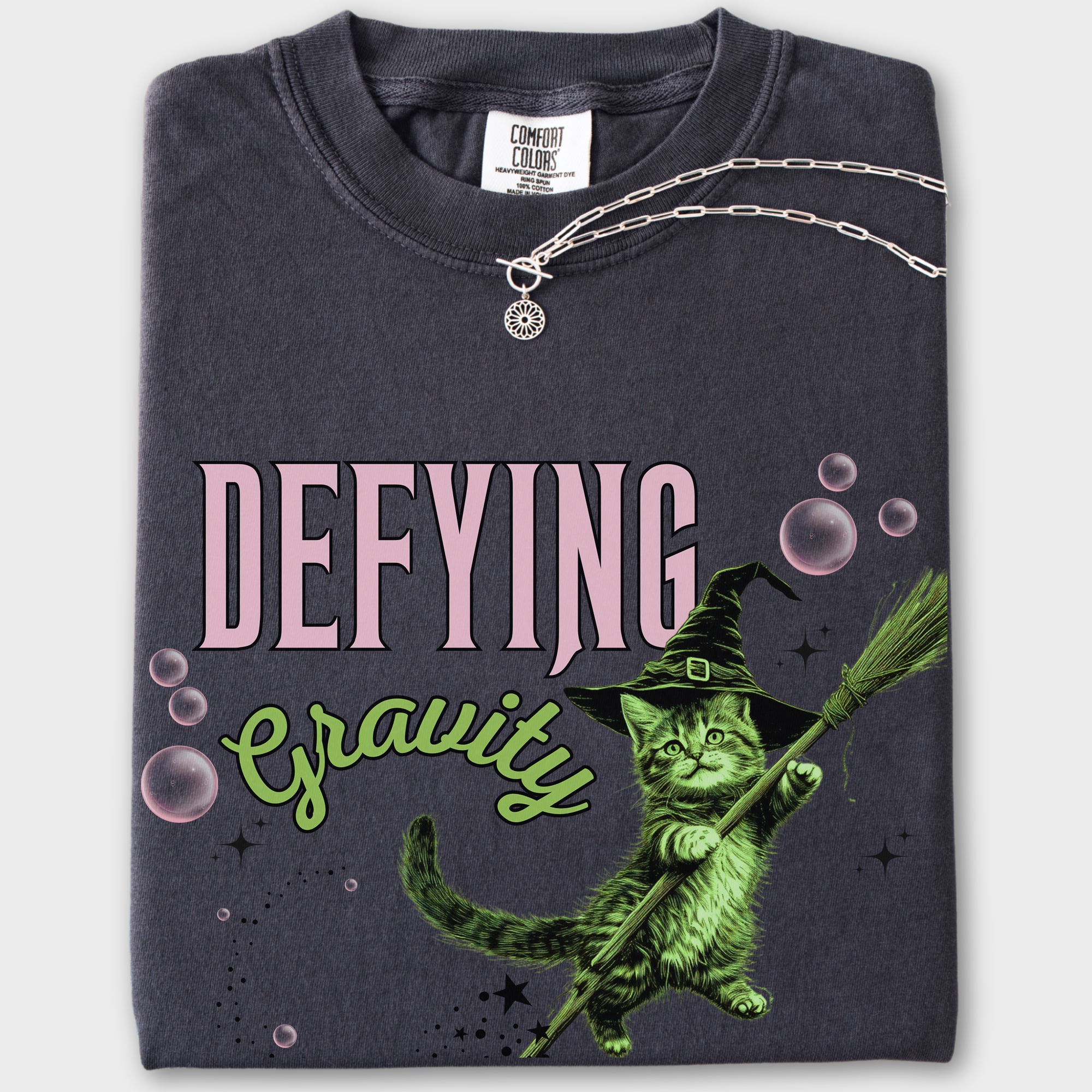 Retro-style cat T-shirt featuring a levitating green witch cat, inspired by Wicked. Unique artwork on soft cotton fabric.