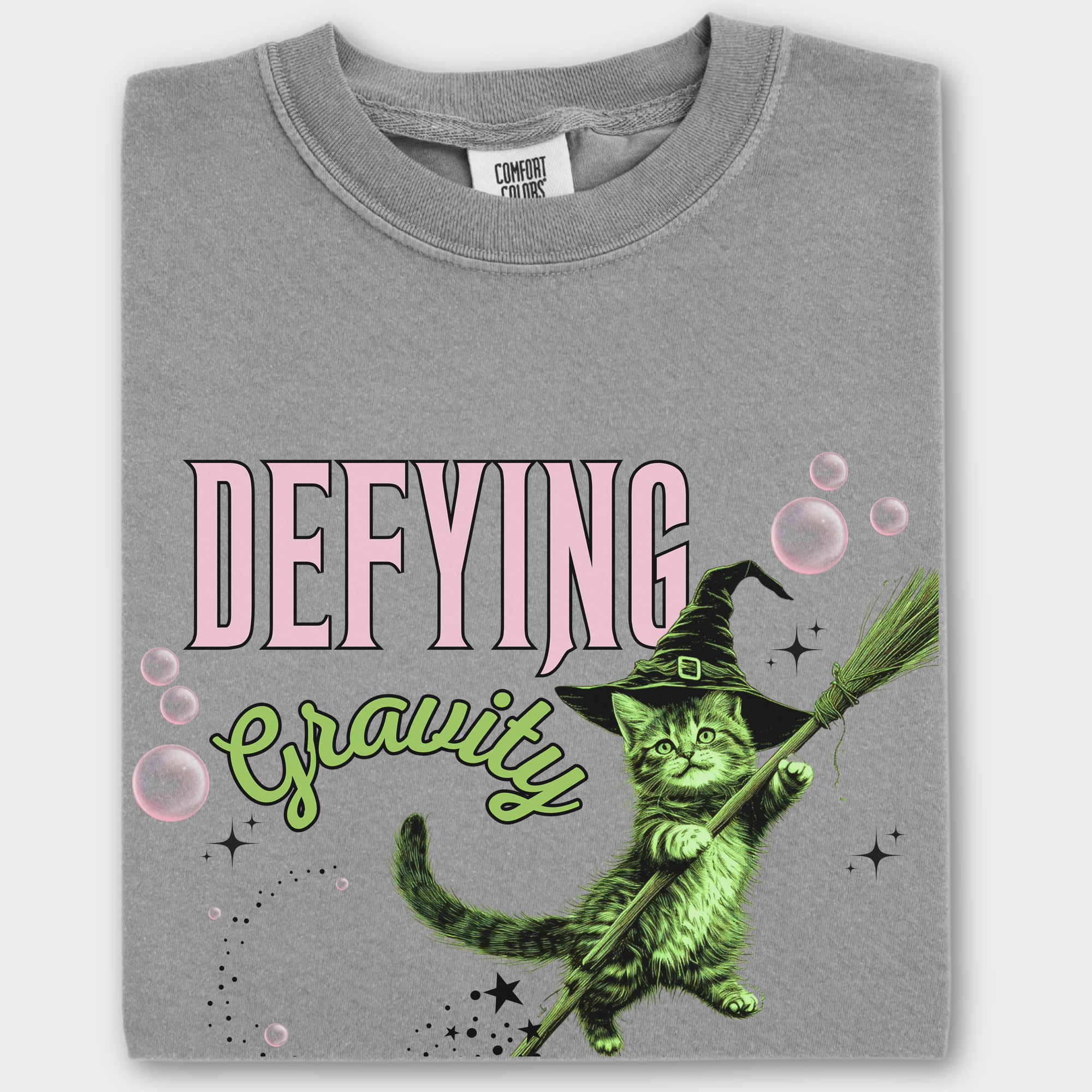 Retro-style cat T-shirt featuring a levitating green witch cat, inspired by Wicked. Unique artwork on soft cotton fabric.