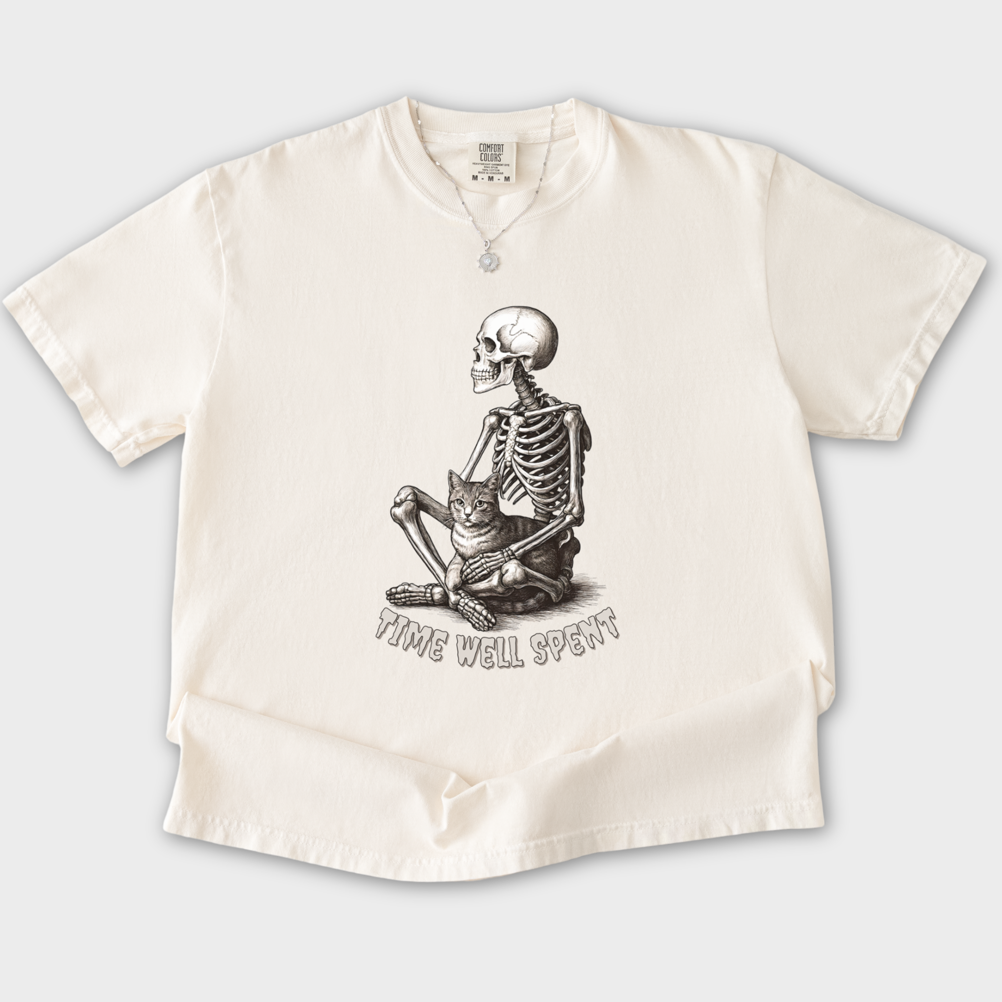line-art-sit-still-skeleton-petting-cat-cat-skeleton-comfort-colors-t-shirt-in-ivory - Ivory Flat Lay Front